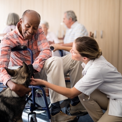 Cheerful female doctor kneeling by disabled senior man stroking puppy Cheerful female doctor kneeling by disabled senior man stroking puppy at retirement home