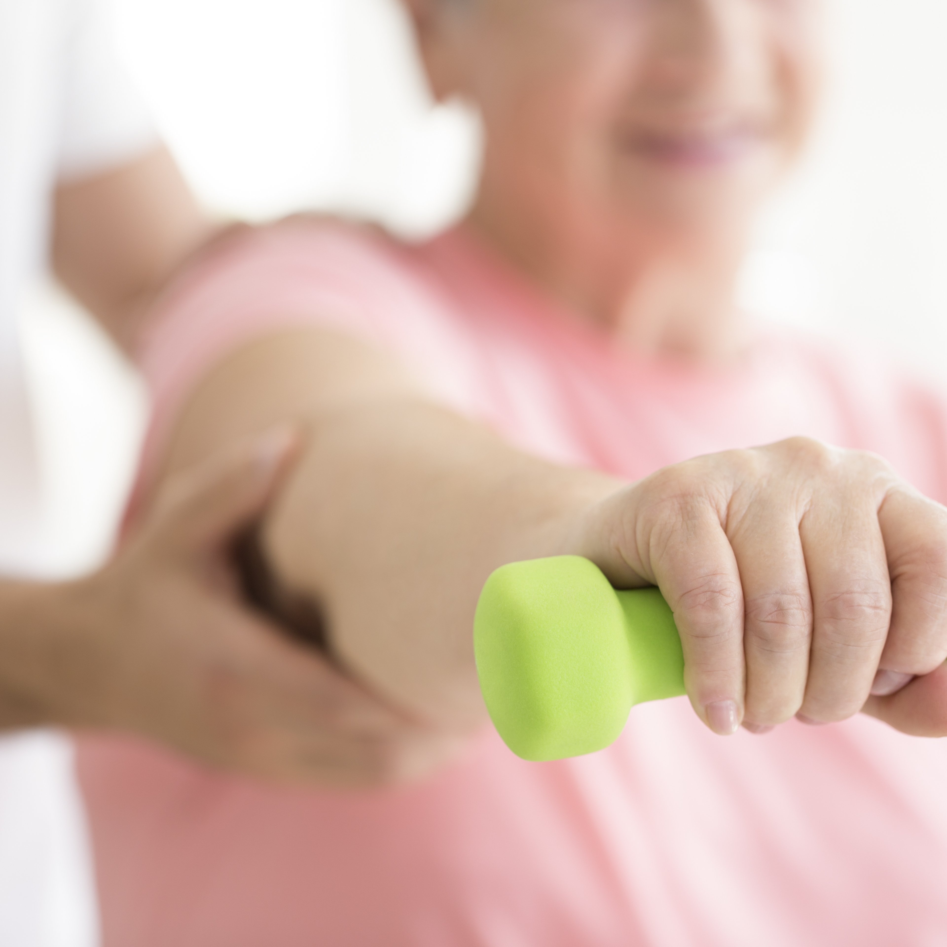 Elderly patient holding a minor dumb-bell in her right hand during isometric physiotherapy